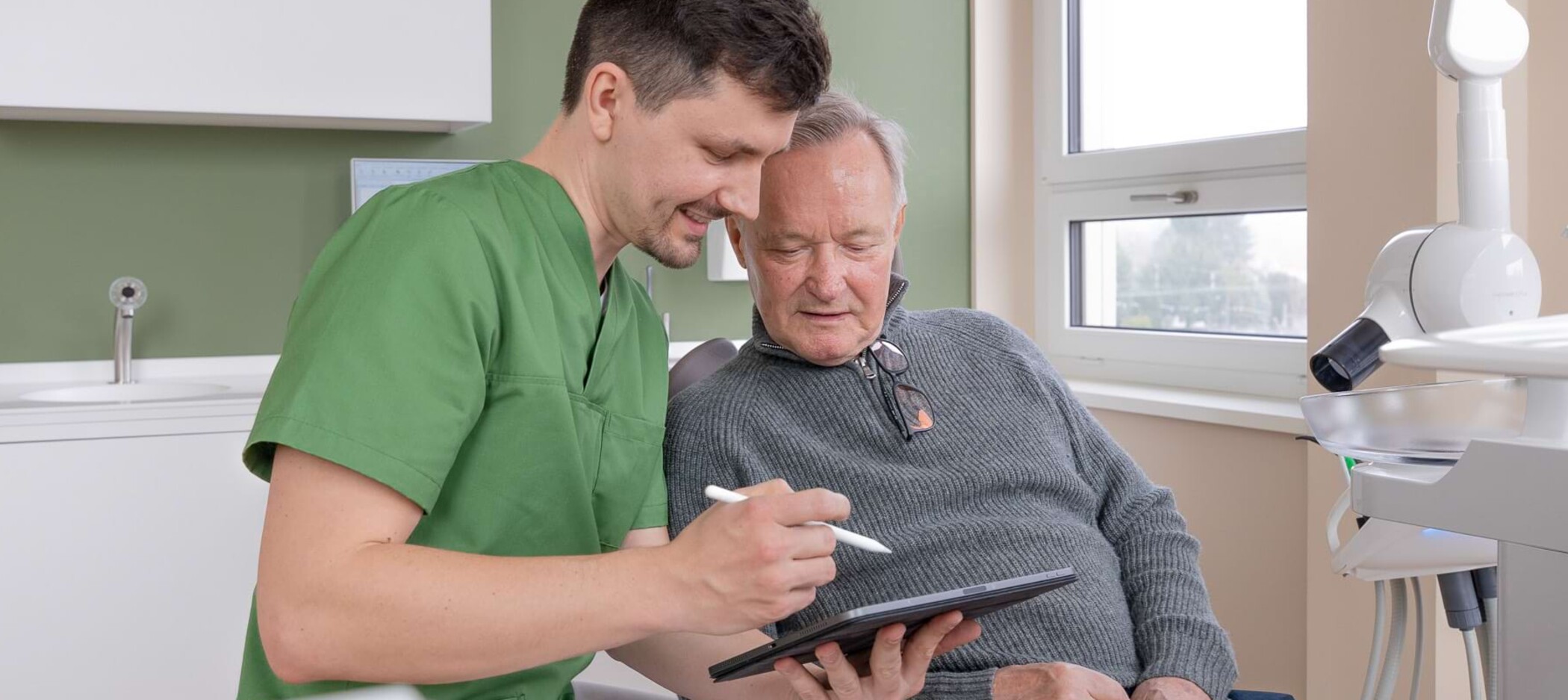 Fotoaufnahme: Christian Schwenn zeigt einem älteren Patienten etwas auf einem Tablet