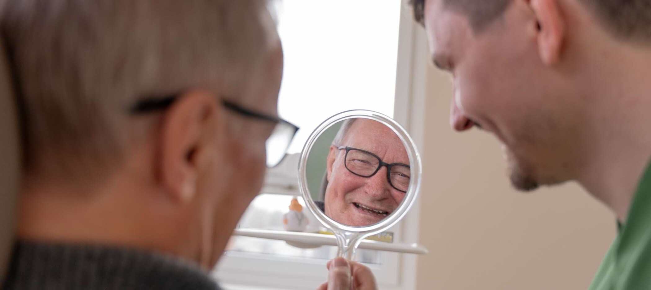 Fotoaufnahme: Patient hält einen Spiegel in der Hand und lächelt, Fokus auf den Spiegel