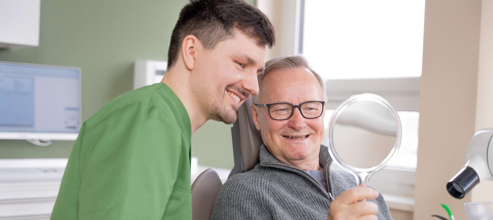 Fotoaufnahme: Christopher Schwenn schaut mit einem Patienten in einen Handspiegel