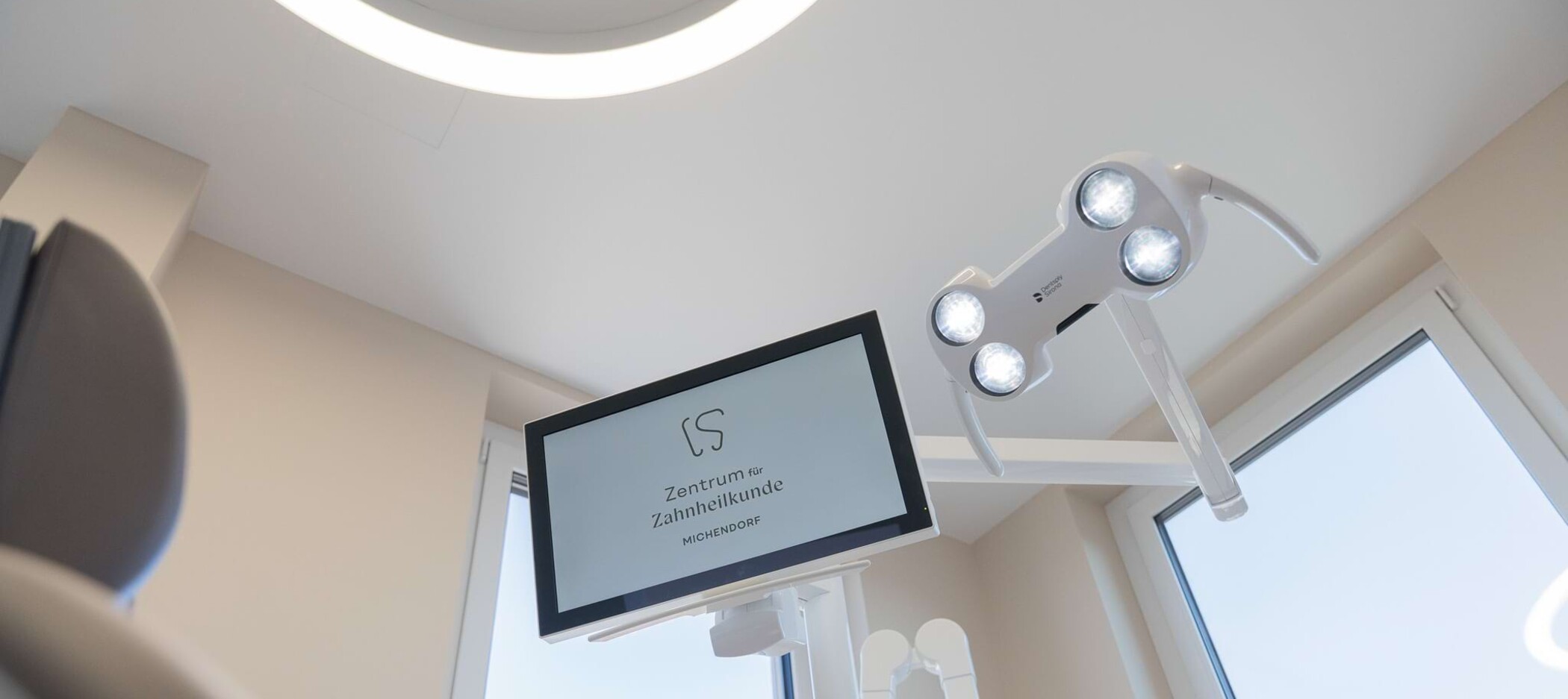 Fotoaufnahme: Behandlungsstuhl und Screen mit Logo Zentrum für Zahnheilkunde Michendorf