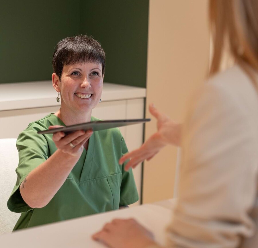 Fotoaufnahme: Mitarbeiterin überreicht Patientin am Empfang Unterlagen